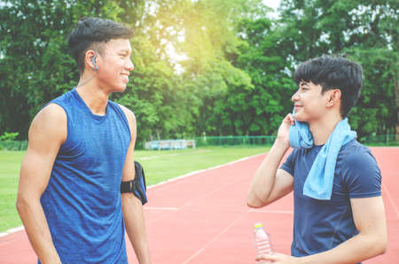 Two Man runners standing talking after running and training exercise in stadium, talking and smiling and drink water while restingの写真素材