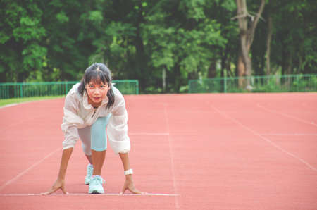 Young woman wearing sports clothes and ready to start running on the track in stadium, sport womenの写真素材