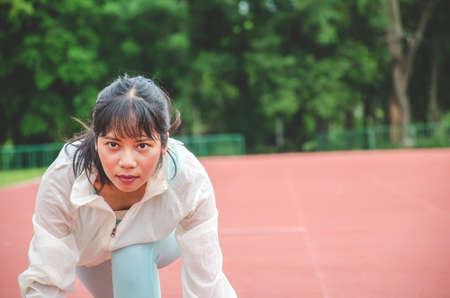 Young woman wearing sports clothes and ready to start running on the track in stadium, sport womenの写真素材