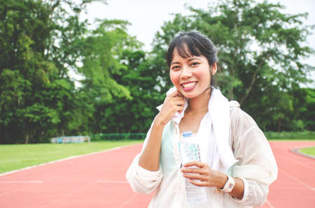 Stunning fitness woman wiping sweat and holding a bottle of water after Jogging outdoors at the stadium in sunny morning, Empty space.の写真素材