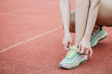 Running shoes - closeup of woman tying shoe laces. Female sport fitness runner getting ready for jogging outdoors on the lanes of a trackの写真素材