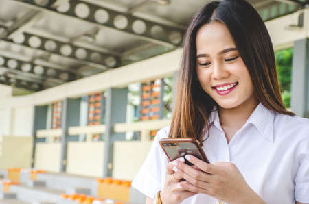 Portrait of thai adult student university uniform beautiful girl is enjoying social media on her...