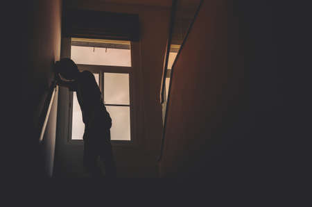 Alone man silhouette standing at the window closed in darkhome. Man stands at window alone, Depression and anxiety disorder concept.の写真素材