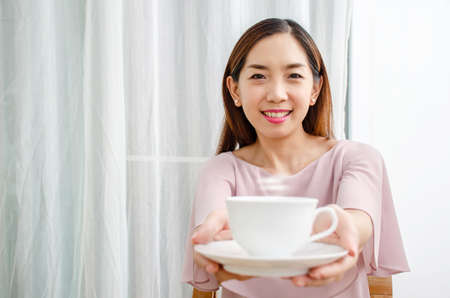 Beautiful smiling young woman hand holding take away coffee cup to her manの写真素材