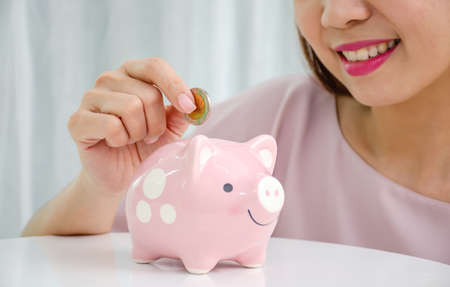 Happy asian woman putting money coin in to piggy for saving money wealth and financial concept.の写真素材