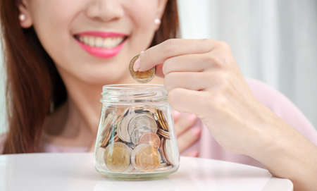 Young woman smile holding coins putting into glass jar, Savings concept for finance accounting at...
