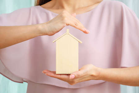 Model of a house on one hand. A second hand is held protectively over it.の写真素材