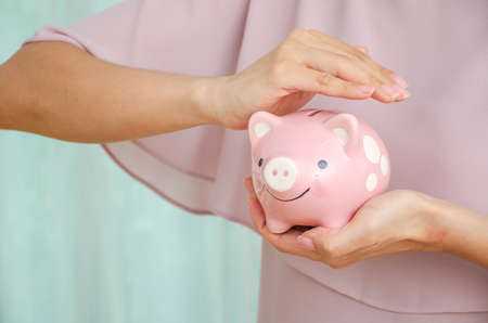 Hands woman holding and protect piggy bank. Savings money, Accounting, business, budget and finance concept.の写真素材