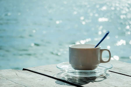 Aromatic coffee white cup in a blurry riverside view landscape background in sunshineの写真素材