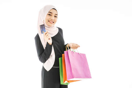 Portrait of beautiful asian muslim woman in a black hijab smiling cheerful with shopping bag and credit card  isolated over white backgroundの写真素材