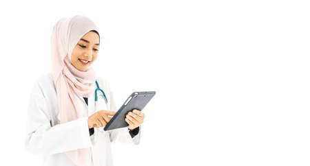 Portrait of beautiful young Muslim woman doctor using digital tablet computer, standing isolated on white backgroundの写真素材