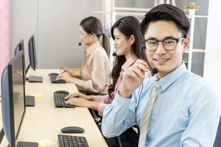 Call center, Service desk consultant talking on hands-free phone, Happy young male customer support executive working in office, Office and business conceptの写真素材