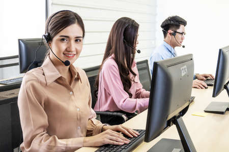 Call center, Service desk consultant talking on hands-free phone, Happy young female customer support executive working in office, Office and business conceptの写真素材