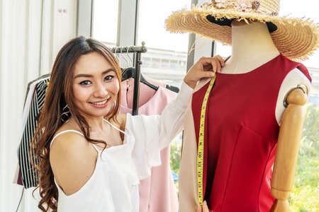 Woman fashion designer measuring a dress, seamstress using tape working with dummy in cozy creative design studio or tailor shop, dressmaking and sewing concept, exclusive unique clothes creationの写真素材