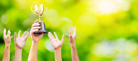 Many hands raised up. Winner is holding trophy cup in hand. on blurred green background