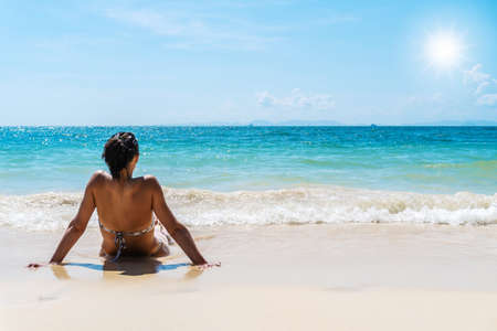 Summer lifestyle of suntanned woman. Enjoying life and sitting back on the beach and sea of the tropical island. Wearing stylish bikini Looking at the sea, relaxing and travel bright sky in thailandの写真素材