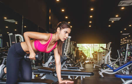 Young beautiful woman doing exercises lifting dumbbell in gym. Girl is enjoying with her training...