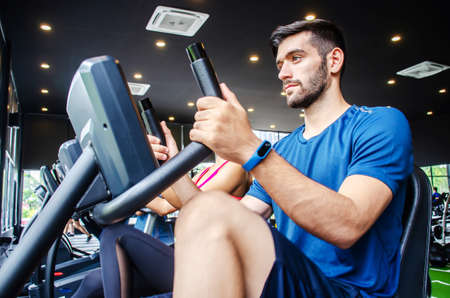 Portrait of young man exercising using stationary bike in gym with a group of people. Fitness class doing sport biking in the gym for health.の写真素材