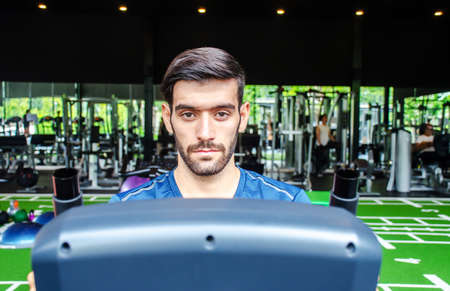 Front view of young man exercising using stationary bike in gym, Fitness class doing sport biking in the gym for health.の写真素材