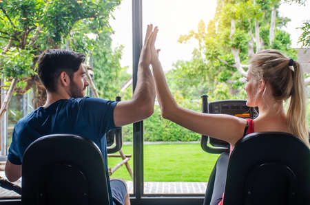 Young sporty woman and man giving each other a high five after cycling training in gym. Fit couple high five after workout in health club, Fitness class doing sport biking in the gym for health.の写真素材