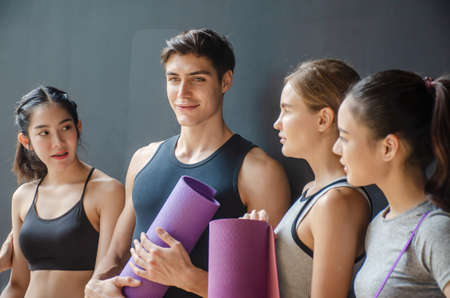 Group of young sporty people with fitness yoga exercise mats standing beside black wall.Students taking a rest from fitness activity, time to recover strength, waiting for a lesson to start in loft studio,Selective focus is manの写真素材