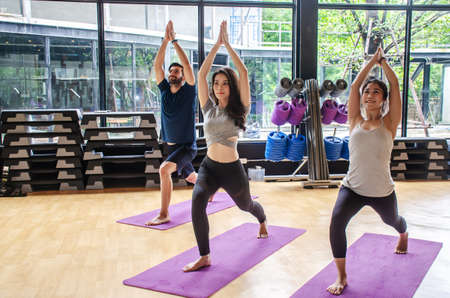 Group yoga in studio concept, diverse multiracial sporty fit people beginners practicing training with instructor teacher standing together trying to repeat warrior 1 poseの写真素材