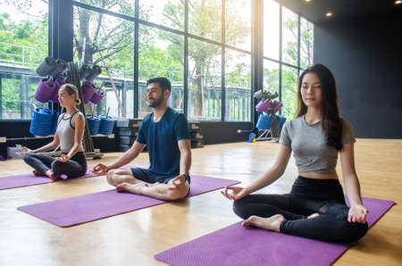 Young yoga practitioners in group doing yoga in modern fitness class indoorの写真素材