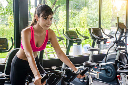 Young sporty woman cycling on bike machine in modern fitness gym,  Workout in Gym and fitness for health.の写真素材