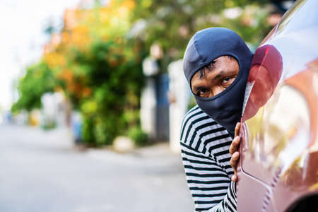 The robber wearing a black head are secretly behind the car to prepare a robbery, Planning a robbery, to crime concept.の写真素材