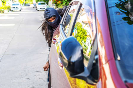 The robber wearing a black head are secretly behind the car To prepare a robbery, Planning a robbery, to crime concept.の写真素材