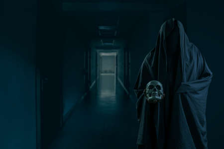 Portrait of a mysterious black man holding a skull in his hand at a creepy hotel corridor