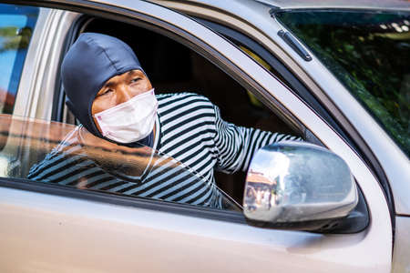 The robber wearing a medical mask has robbed the car and sat in the car with the window and door open to see the incident, Concept of crime growth in the context of the coronavirus crisisの写真素材