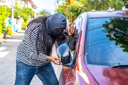 Hair long Male thief wearing black robbery mask trying to open car window with ruler, Car thief concept.の写真素材