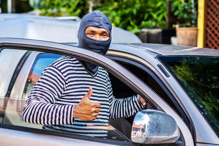The male thief wears a black and white striped shirt and wears a black mask, smiling happily after...