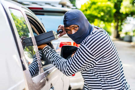 Transportation, crime and ownership concept -Young asian man thief stole a leather bag from a car whose windowsの写真素材