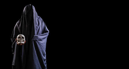 Portrait of a mysterious black man holding a skull in his hand isolated on black background,Portrait of a mysterious black man holding a skull in his hand isolated on black background, Devil or Satan take soul or spirit from dead man. Horror movie , spooky novelの写真素材
