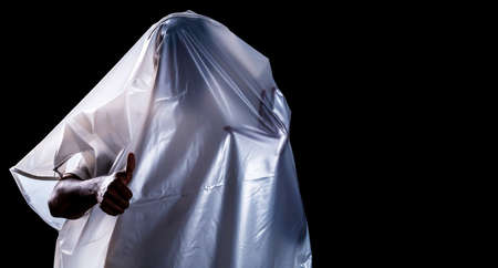 A man covered with a white shroud like a ghost shows a thumb up isolated on black background with copy space,Halloween and horror,with clipping pathの写真素材