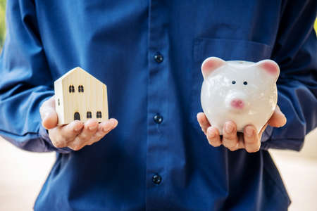 Man holding piggy ceramic bank and model home in hand for finance and banking, Real estate or home savings concept.の写真素材