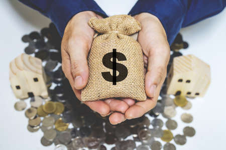 Man hand hold a money bag on the home model put on the coins, Saving money for buy house or loan for investment of real estate concept for future investment concept.の写真素材