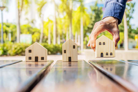 Hand choosing wood house model from group of house on table, Real estate concept, planning to buy property, mortgage, investment, A symbol for construction ,ecology, loan concepts,selective focusの写真素材
