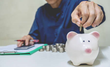 Saving money concept,Man hand putting coin drop into piggy bank and accounting calculate calculator expenses with savings money coins stacked row,save money concept, concept Write Finance accountingの写真素材
