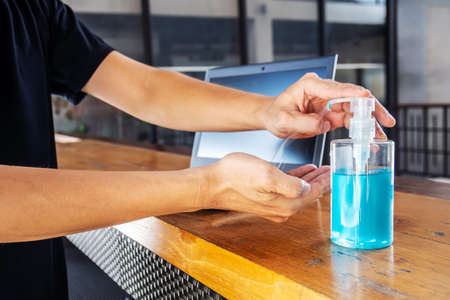 Closeup Asian man using hand sanitizer by pumping alcohol gel and washing before start to work with laptop in office period,Clear sanitizer in pump bottle, for killing germs, bacteria and virusの写真素材