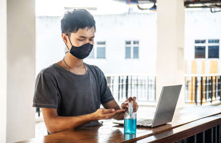 Asian man using hand sanitizer by pumping alcohol gel and washing before start to work with laptop in office period,Clear sanitizer in pump bottle, for killing germs, bacteria and virusの写真素材