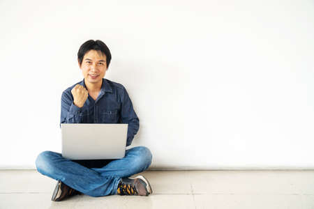 Young man asian sitting on the floor with using computer laptop happy excited with big smile posing isolated over white wallの写真素材