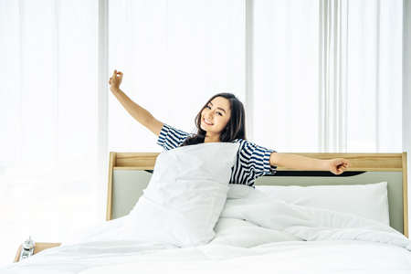 Beautiful young woman stretching in bed with her arms raised after wake up,  Healthy lifestyle, Wellness conceptの写真素材