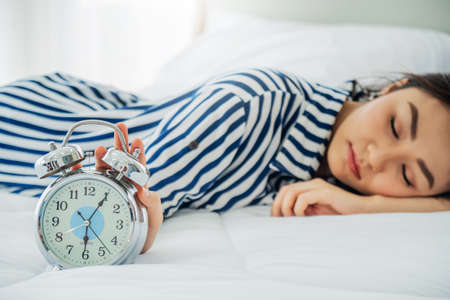 Asian young beauty woman sleeping and her hand touching turning off alarm clock in Morning . Lazy time and Holiday concept. Bedroom theme.の写真素材
