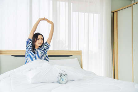 Beautiful young woman stretching in bed with her arms raised after wake up,  Healthy lifestyle, Wellness conceptの写真素材