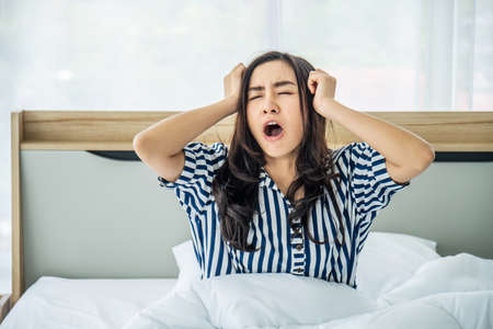 Sleepy young woman sitting and yawning after she wake up in bed at homeの写真素材