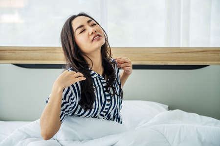 Young asian girl happy stretching in bed after wake up in the morning. Portrait of beautiful asian woman enjoying fresh soft bed linen mattress in bedroom.の写真素材