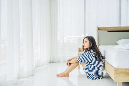 Beautiful asian woman sitting on the floor near bed feeling depressed stress in bedroom, Young woman suffers from insomniaの写真素材